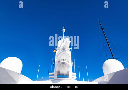 Grand mât d'un yacht avec équipement de navigation, vue d'en bas. Radars, feux de signalisation, antennes paraboliques et équipements avec le drapeau de l'Espagne. Banque D'Images