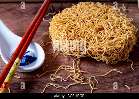 Gros plan de nouilles de blé chinoises fines séchées avec une cuillère en céramique et une paire de baguettes. Banque D'Images