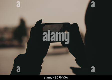 Silhouette d'une personne prenant une photo d'un bâtiment avec un smartphone. Une personne est silhouettée sur un fond flou, tenant un téléphone pour capturer Banque D'Images
