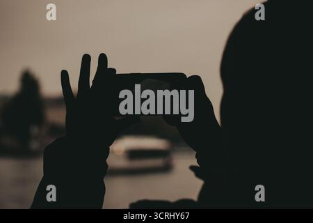Silhouette d'une personne prenant une photo d'un bâtiment avec un smartphone. Une personne est silhouettée sur un fond flou, tenant un téléphone pour capturer Banque D'Images