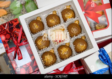 Une sélection de chocolats faits à la main dans des coffrets cadeaux. Gros plan d'un coffret cadeau contenant des gâteaux nappés de chocolat et des saupoudrés de couleurs vives Banque D'Images