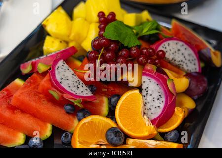 Plateau de fruits tropicaux vibrant pour un rafraîchissement estival. Gros plan d'un plateau de fruits coloré avec pastèque tranchée, fruit du dragon, ananas, orange Banque D'Images