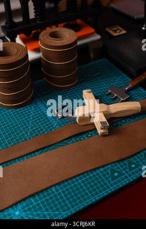 Installation de travail du cuir avec des outils, une boucle et des bandes de cuir disposées soigneusement sur un tapis, prêt pour la fabrication de ceinture. Outils de maroquinerie et fabrication de courroies p Banque D'Images