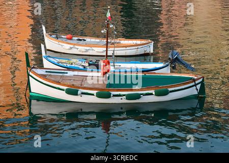 Trois petits bateaux de pêche ancrés dans le port avec des reflets d'eau au coucher du soleil, Camogli (Gênes), Ligurie, Italie Banque D'Images