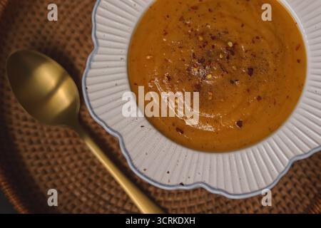 Soupe de citrouille chaude dans un bol garni de flocons de piment, prête à manger, servie sur un tapis tissé. Concept de nourriture d'automne réconfortant Banque D'Images