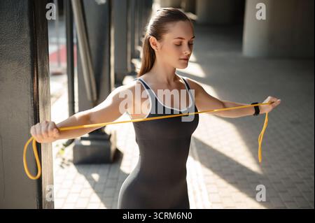 Femme sportive concentrée s'exerçant avec une bande de résistance jaune à l'extérieur Banque D'Images
