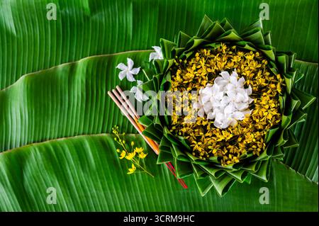 Krathong décore avec des fleurs blanches et jaunes qui ont flou le focus de 3 bâtons d'encens et bougie mis sur la feuille de banane pour le festival Loy Krathong. Banque D'Images