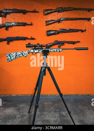 THE BALTICS - 30 SEPTEMBRE 2025 : un ruger de fusil de sniper 22lr avec un suppresseur sur un trépied devant un mur avec diverses armes à un champ de tir. Banque D'Images
