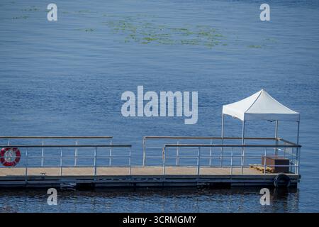 Jetée flottante vide avec des rampes de sécurité et une canopée blanche se dresse sur un lac calme avec de douces ondulations, sous la lumière du jour dans un cadre d'été calme Banque D'Images