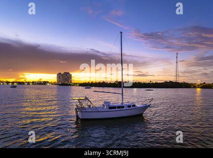 Vue aérienne d'un voilier solitaire flottant sur Biscayne Bay alors que le soleil couchant peint le ciel dans des teintes flamboyantes derrière les bâtiments, Miami, Floride, États-Unis. Banque D'Images