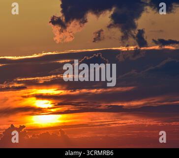 Ciel crépusculaire enchanté avec des nuages pastel vifs, brillants par le soleil caché derrière, créant une atmosphère onirique paisible. Banque D'Images