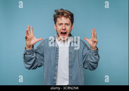 Homme exprimant la frustration avec les mains levées dans un cadre de fond bleu Banque D'Images
