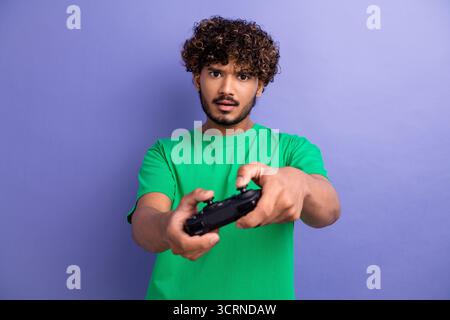 Jeune homme portant une chemise verte tenant le contrôleur de jeu sur un fond violet représentant le jeu et les loisirs Banque D'Images
