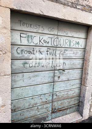 Graffiti sur une porte croate proteste contre le tourisme et la corruption, reflétant le mécontentement local et les tensions sociopolitiques dans l'espace urbain Banque D'Images