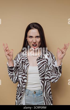 Une jeune femme montre sa frustration avec une expression intense tout en portant une chemise à motifs noir et blanc tendance et un Jean décontracté. Son drame Banque D'Images