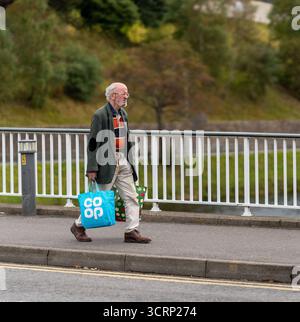 C'est un homme marchant à travers la rivière Ness à Inverness, portant 2 sacs à provisions. Banque D'Images