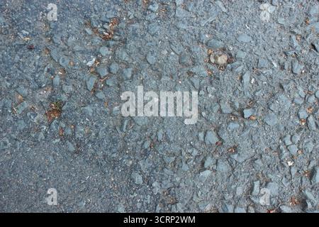 Gros plan de la texture du sol en asphalte avec des pierres rugueuses et de petits débris, fond de chaussée urbaine Banque D'Images