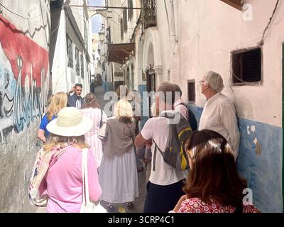 Les ruelles sont étroites et sinueuses dans les zones historiques des villes médiévales nord-africaines et arabes. Les touristes aiment marcher dans une médina ou un souk car ils offrent beaucoup de culture et d'histoire. Un jeune homme local guide un groupe de touristes anglais à travers la vieille ville de Tanger, au Maroc. Banque D'Images
