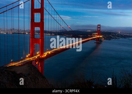 Une photo en exposition longue du Golden Gate Bridge la nuit, montrant les traînées lumineuses des voitures traversant le pont. Banque D'Images
