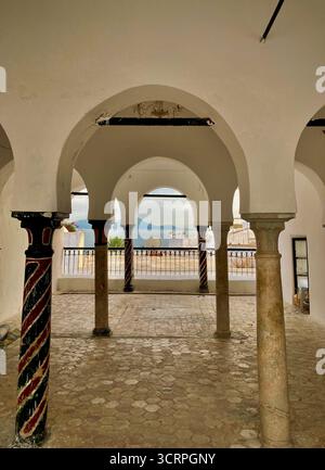 Scène de rue bleue et blanche à Sidi Bou Said, Tunisie : art mural en céramique, chemin pavé et sièges de café. Capturé le 23 septembre 2025. Banque D'Images