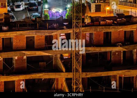 Un gros plan détaillé d'un bâtiment en briques inachevé à Benidorm la nuit. La structure brute, avec ses planchers exposés et son encadrement, est éclairée Banque D'Images