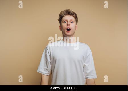 portrait du jeune homme surpris a la bouche ouverte dans l'étonnement, soulignant un moment de choc sur fond beige Banque D'Images