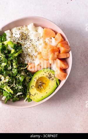 Un bol de petit-déjeuner nutritif composé de riz, de saumon, d'avocat et de légumes frais est présenté magnifiquement dans un bol. Idée de repas du matin simple et sain Banque D'Images