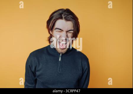 Jeune homme aux cheveux longs riant sur fond orange. Banque D'Images