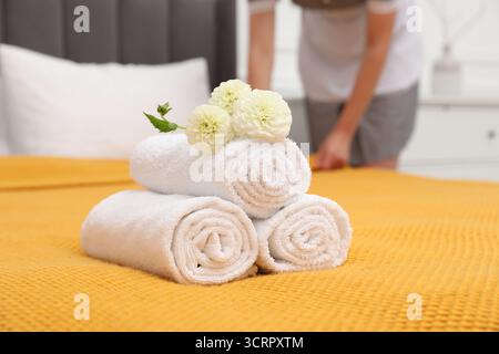 Femme de chambre travaillant dans la chambre d'hôtel, se concentrer sur les serviettes éponges roulées et les fleurs de dahlia sur le lit Banque D'Images