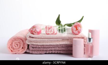 Pile de serviettes éponge fraîches, de produits cosmétiques et de fleurs isolées sur blanc Banque D'Images