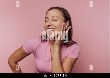 La jeune femme sourit et pose de manière ludique sur un fond rose solide, créant une atmosphère vibrante et joyeuse qui met en valeur sa joyeuse personnalité Banque D'Images
