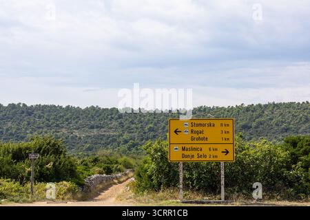 Un panneau routier jaune vif se trouve dans une campagne croate paisible, pointant vers Stomorska, Rogac, Grohote, Maslinica et Donje Selo. Roulis Banque D'Images