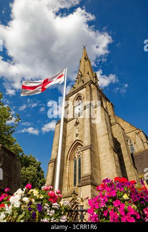 La flèche de l'église paroissiale s'élève dans un ciel bleu avec un affichage de fleurs aux couleurs vives sous un drapeau de l'Union Jack, Bury, Greater Manchester. Banque D'Images