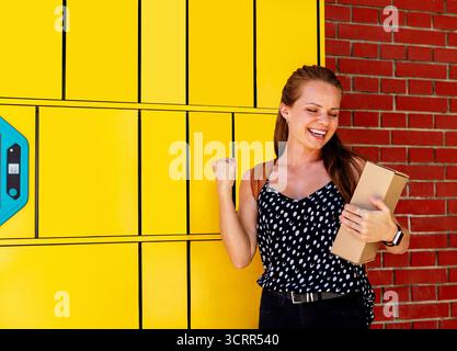 Femme joyeuse collectant le paquet du casier à colis automatisé à l'extérieur Banque D'Images