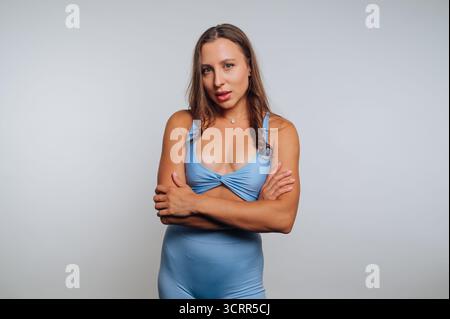 Une jeune femme se tient debout, les bras croisés, présentant une tenue bleu clair. Elle semble confiante et détendue dans un décor studio minimaliste, highlig Banque D'Images