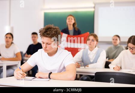 Un enseignant du secondaire parle aux élèves du Danemark et détient un drapeau du Danemark entre les mains. Banque D'Images