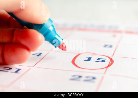 Main féminine dessinant un cercle rouge avec un marqueur sur une page de calendrier. Concept commercial. Banque D'Images