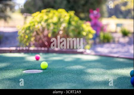 Balles de golf colorées sur un parcours de mini-golf avec un fond vibrant par temps ensoleillé Banque D'Images