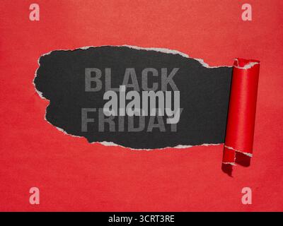 Papier rouge avec une grande déchirure, révélant un fond noir sur lequel sont imprimés les mots « Black Friday » Banque D'Images