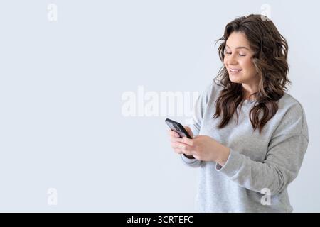 Belle femme européenne en costume tricoté gris souriant et regardant la vidéo sur son smartphone. Banque D'Images