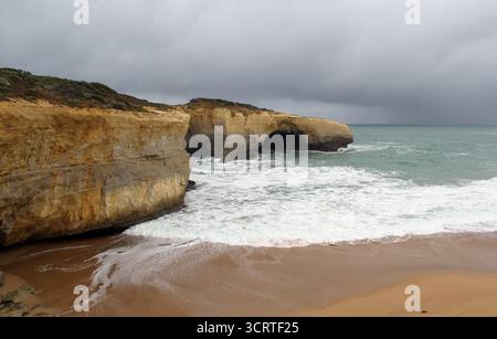 Formation rocheuse de London Arch avec vagues océaniques, plage de sable et ciel nuageux sur la Great Ocean Road à Victoria, en Australie Banque D'Images