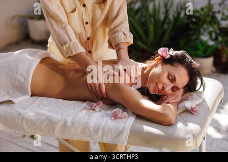 Massage du dos en plein air dans un spa de jardin avec lumière naturelle, soulageant le stress et favorisant le bien-être calme. Banque D'Images