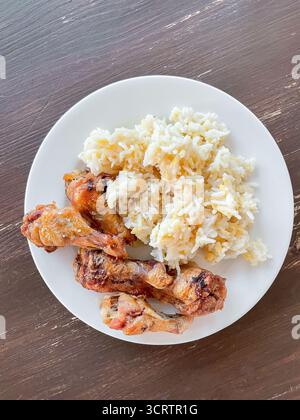 Des ailes de poulet croustillantes cuites au four sont servies avec du riz moelleux et des lentilles cuites sur l'assiette. Porte-plats sur une table en bois rustique Banque D'Images