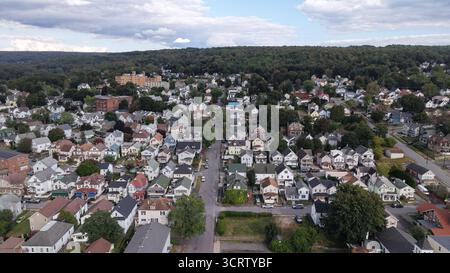 Vue aérienne des toits se mélangeant du gris ardoise à la terre cuite chaude, niché parmi les arbres luxuriants avec un grand bâtiment au loin, Carbondale, Pennsylvanie, États-Unis. Banque D'Images
