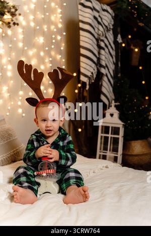 Un enfant vêtu d'un costume de renne fait maison est assis sur un lit, tenant une bouteille de lait Banque D'Images