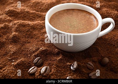 Tasse à café en céramique blanche remplie de café mousseux sur un fond de café moulu et de grains autour. Vue surélevée. Banque D'Images