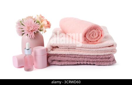 Pile de serviettes éponge fraîches, de produits cosmétiques et de fleurs isolées sur blanc Banque D'Images