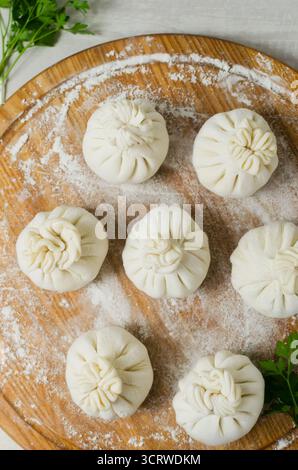 Khinkali cru au persil sur une planche à découper ronde avec de la farine sur la table. Concept de cuisine géorgienne traditionnelle. Orientation verticale. Sélect. F Banque D'Images