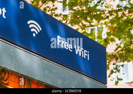 Un panneau bleu « WiFi gratuit » avec un symbole WiFi placé contre les arbres et les bâtiments Banque D'Images