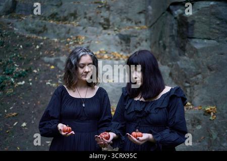 Deux femmes en robes longues noires près des rochers noirs sur Halloween avec des bougies en forme de citrouilles, effectuant un rituel de sorcière, sorcière moderne Banque D'Images